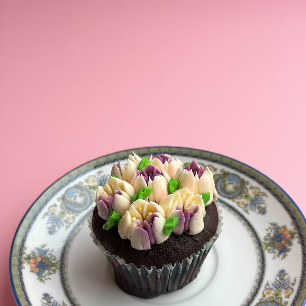 Chocolate cupcake with colorful frosting on a decorative plate against a pink background