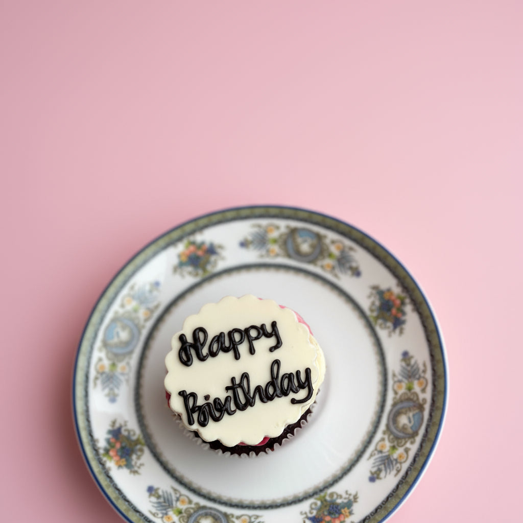 Cupcake with 'Happy Birthday' on a decorative plate against a pink background