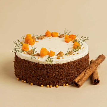 Carrot cake with white frosting, carrots, and cinnamon sticks on a beige background