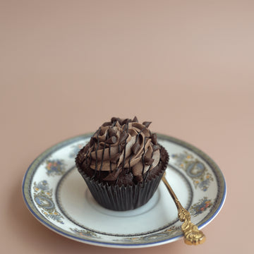 Chocolate cupcake on a decorative plate with a gold spoon against a pink background