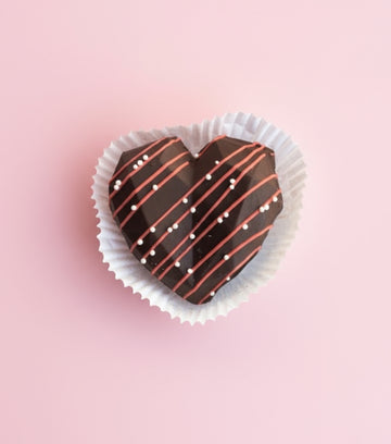 Heart-shaped chocolate treat with white and red drizzle on a pink background