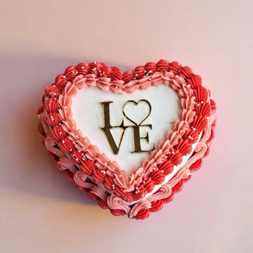 Heart-shaped cake with red and pink frosting and 'I LOVE' text on a soft pink background