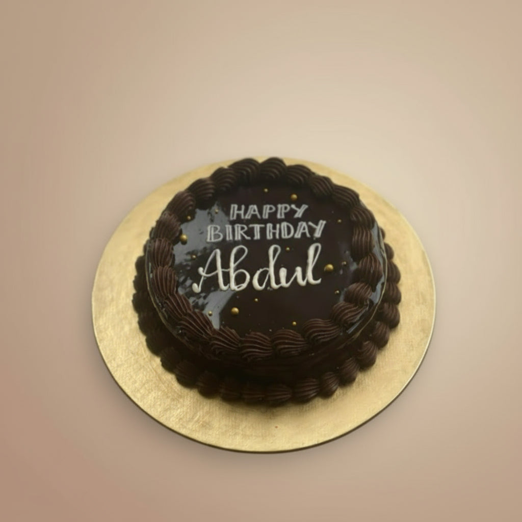 Chocolate birthday cake with 'Happy Birthday Abdul' text on a gold plate against a beige background