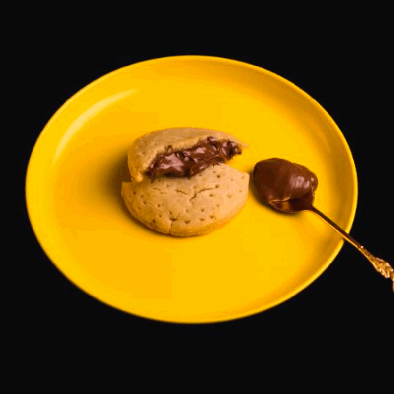 Nutella filled inside crunchy cookie with a spoon of nutella on the side
