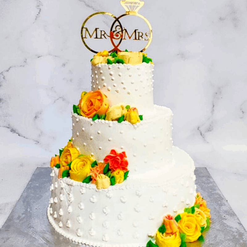 Butter cream drops on each layer of the three-tier wedding cake with the Mr and Mrs Cake topper with yellow buttercream roses