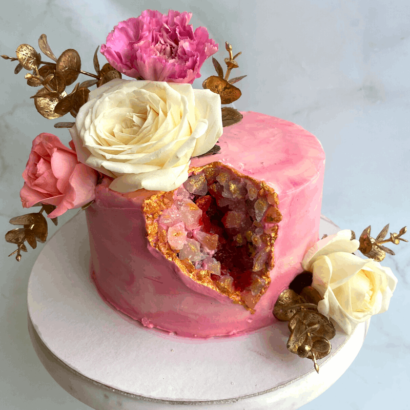 Pink geode cakes spray painted pink and cream with roses decorating its sides