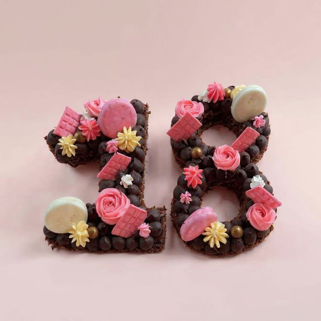 Decorative number '18' cake with chocolate, flowers, and candies on a pink background