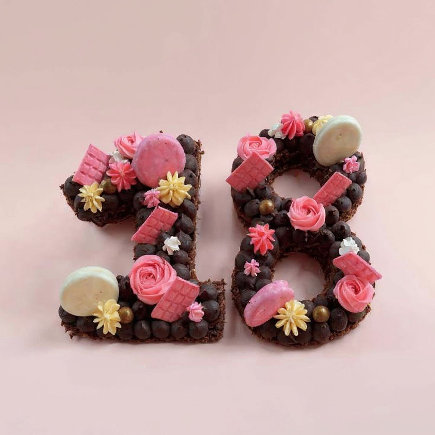 Decorative number '18' cake with chocolate, flowers, and candies on a pink background