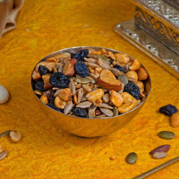 Metallic bowl filled with a mix of dried fruits and nuts on a textured yellow surface.
