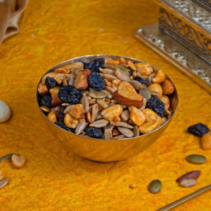 Metallic bowl filled with a mix of dried fruits and nuts on a textured yellow surface.