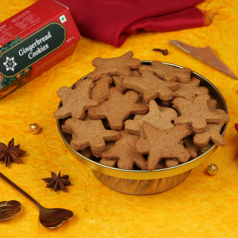 Man-shaped gingerbread cookies in a metal bowl with a box labeled 'Gingerbread Cookies' on a yellow background.