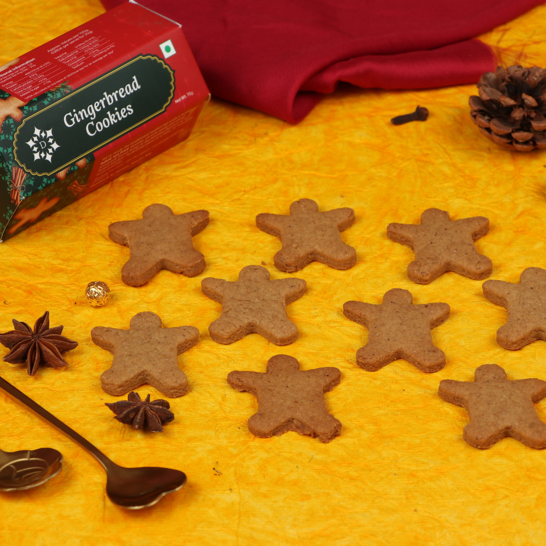 Man-shaped gingerbread cookies on a yellow surface with a box labeled 'Gingerbread Cookies' and pine cones.