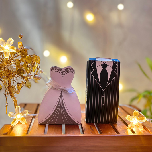 Elegant bride and groom wedding favor boxes with 100% eggless heart-shaped chocolates – two dark cookie crunch and two milk crackles in each. Perfect budget-friendly marriage gift with PAN India shipping, set on a wooden table with fairy lights and golden floral decor