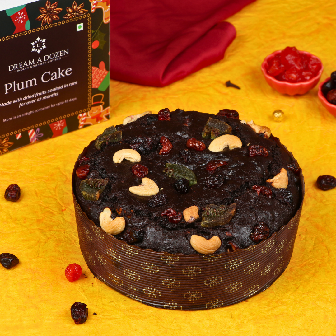 Plum cake with dried fruits on a yellow surface, next to a box labeled 'Dream a Dozen Plum Cake'.
