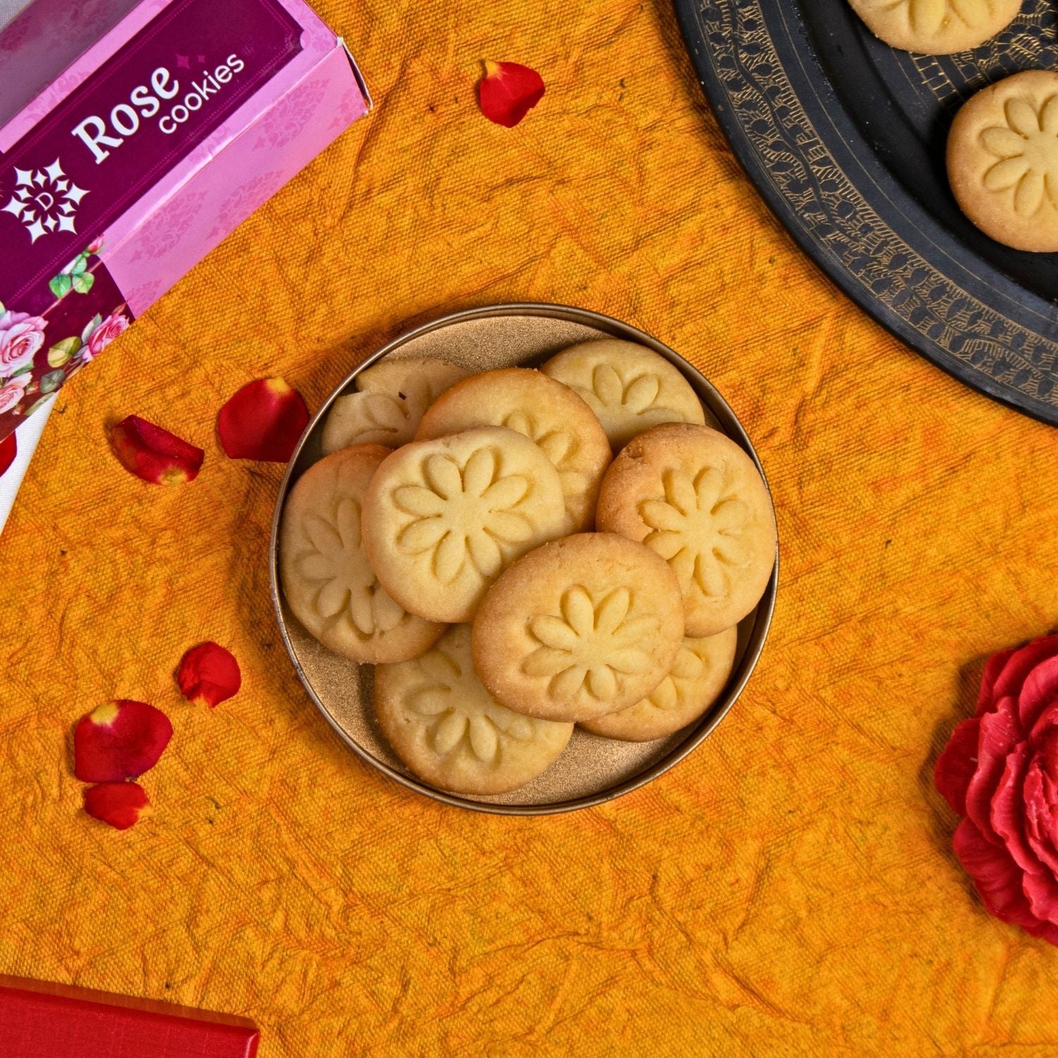Rose cookies in a tin with a box labeled 'Rose cookies' on an orange surface.