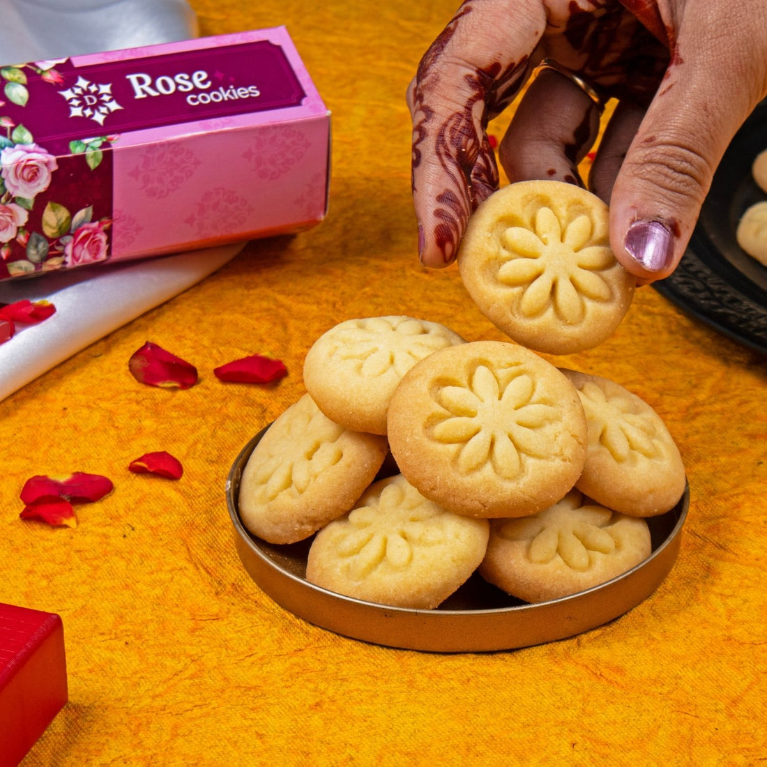 Rose cookies in a tin with a box labeled 'Rose cookies' on an orange surface.