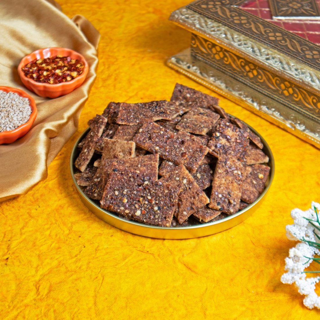Millet crackers in a metal tray on a yellow textured surface with decorative elements.