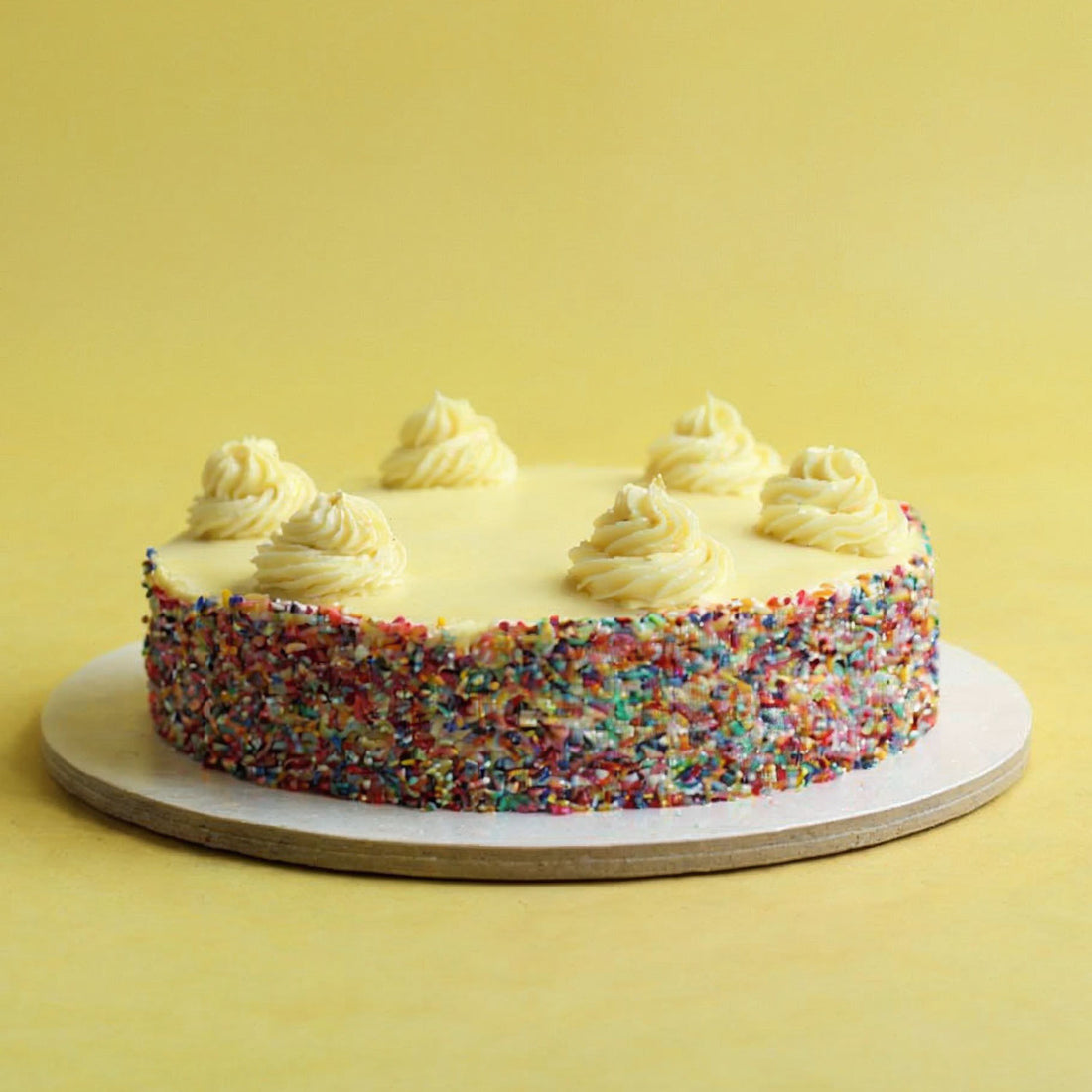 Colorful sprinkled cake with white frosting on a yellow background