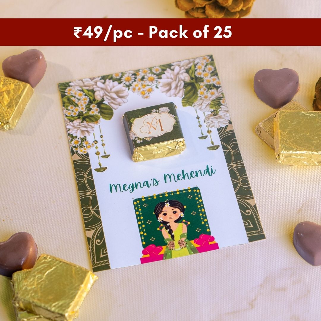 a top down shot of a gorgeous green card with flowers on the top and the bride below with a square chocolate wrapped in green on it 
tasty looking heart shape chocolates that are the perfect wedding gifts are around the card
at just ₹49 per piece this is sold in a pack of 25