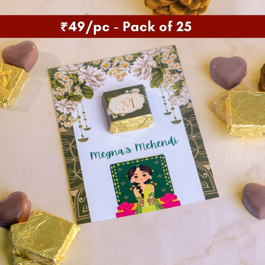 a top down shot of a gorgeous green card with flowers on the top and the bride below with a square chocolate wrapped in green on it 
tasty looking heart shape chocolates that are the perfect wedding gifts are around the card
at just ₹49 per piece this is sold in a pack of 25