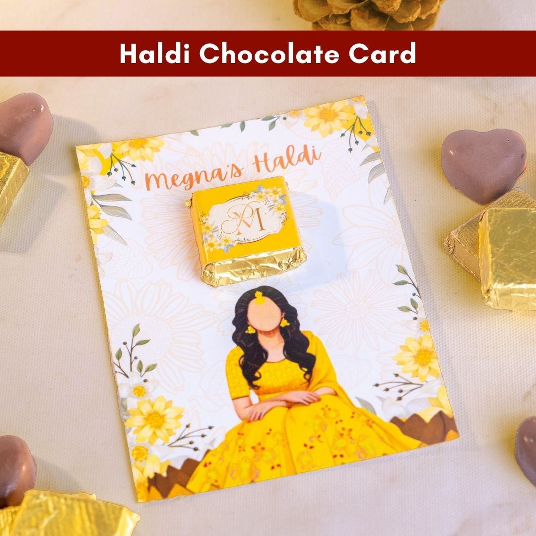 a top down shot of a beautiful yellow card with flowers along the border and a girl in a yellow lehenga in the bottom centre with a bright yellow chocolate above 
there are tasty looking bite sized chocolates made for wedding gifting around the card