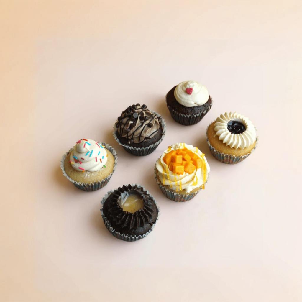 Six small cupcakes with various flavors and toppings on a light background