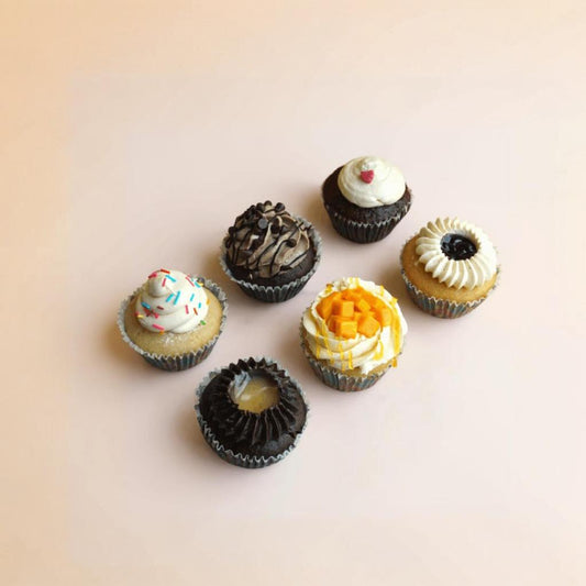 Six small cupcakes with various flavors and toppings on a light background