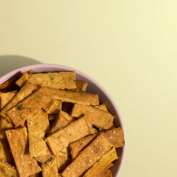 Pink bowl filled with baked mathri on a light yellow background