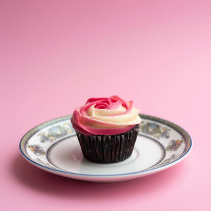 Cupcake with pink and white frosting on a decorative plate against a pink background