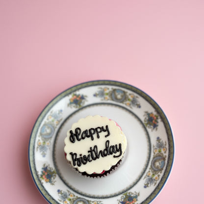 Cupcake with 'Happy Birthday' on a decorative plate against a pink background