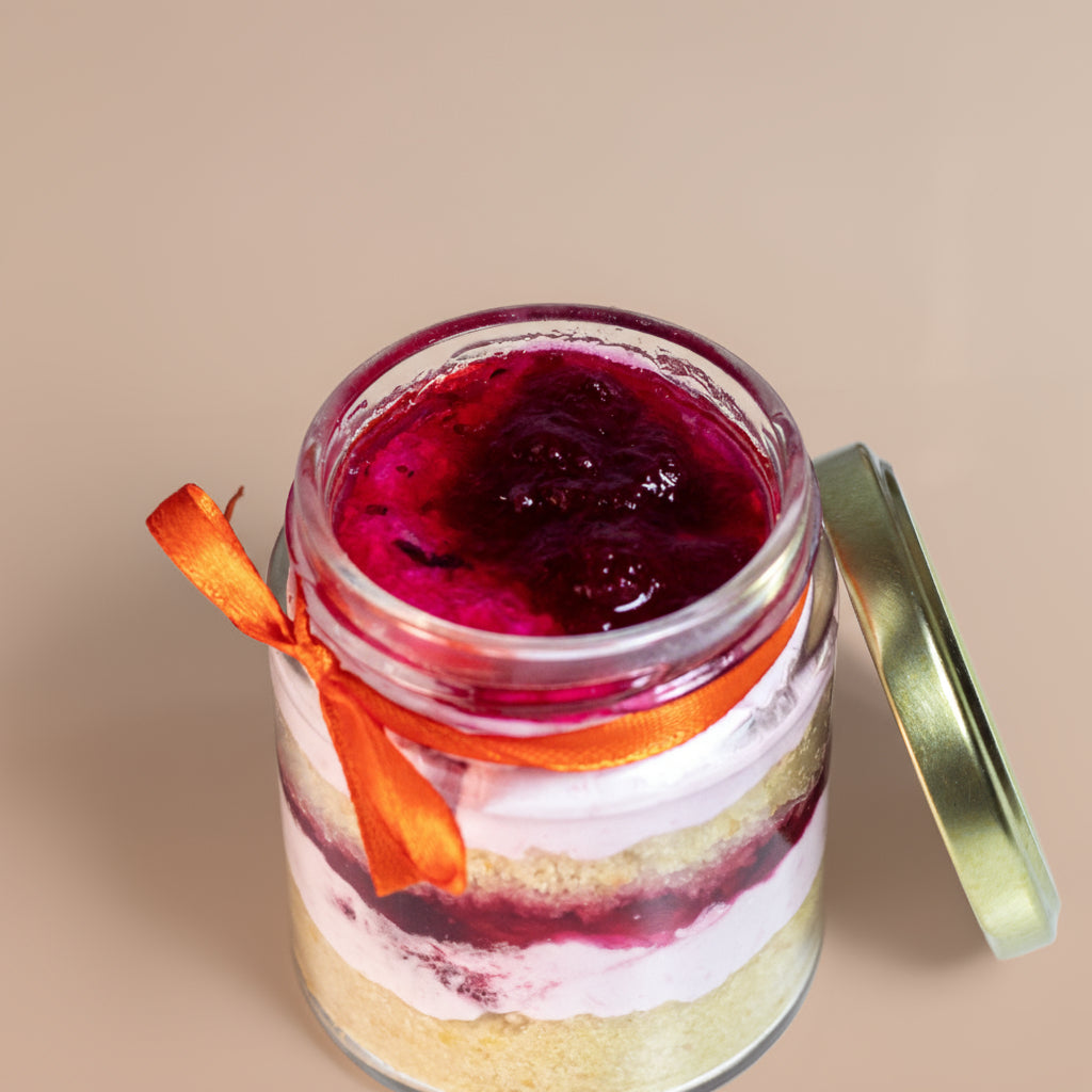 Layered berry dessert in a glass jar with a gold lid on a beige background