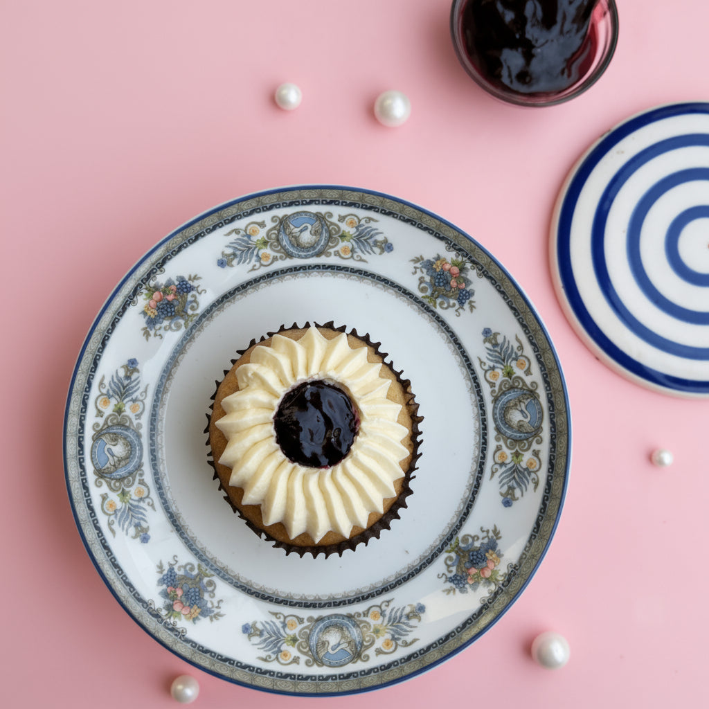 Four blueberry cupcakes with white frosting and a dark center on a pink background