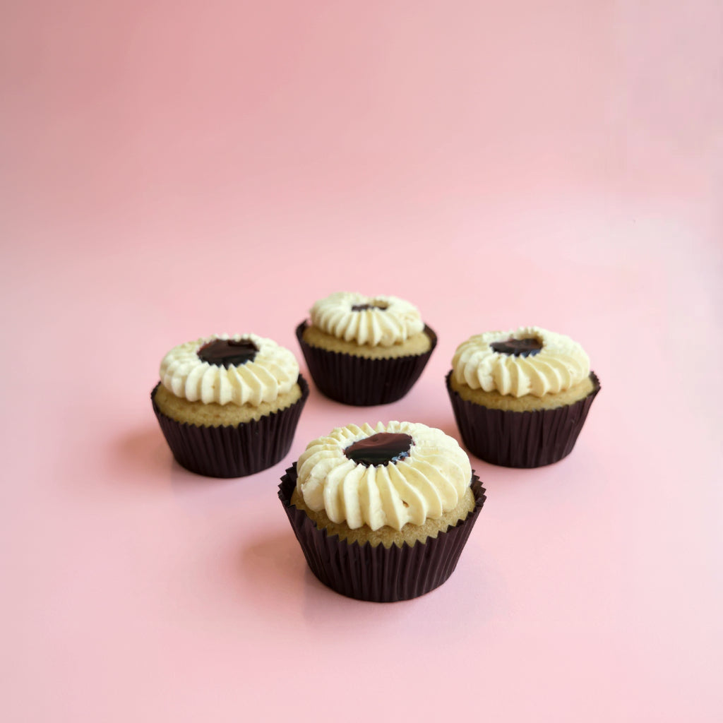 Four blueberry cupcakes with white frosting and a dark center on a pink background