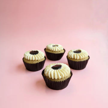 Four blueberry cupcakes with white frosting and a dark center on a pink background