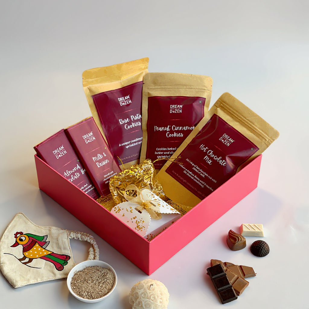 Assorted food items including cookies and chocolate mix in a decorative box with gold ribbons and chocolates.