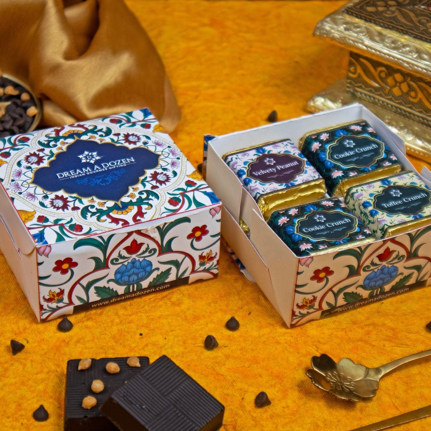 Chocolate bars in decorative boxes on a yellow surface with a spoon and chocolate pieces.