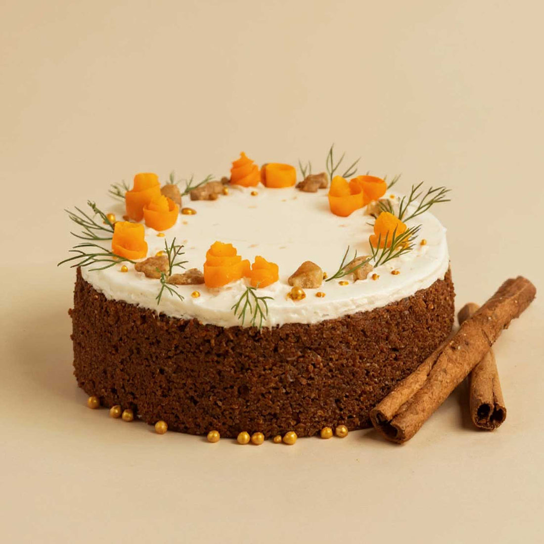 Carrot cake with white frosting, carrots, and cinnamon sticks on a beige background