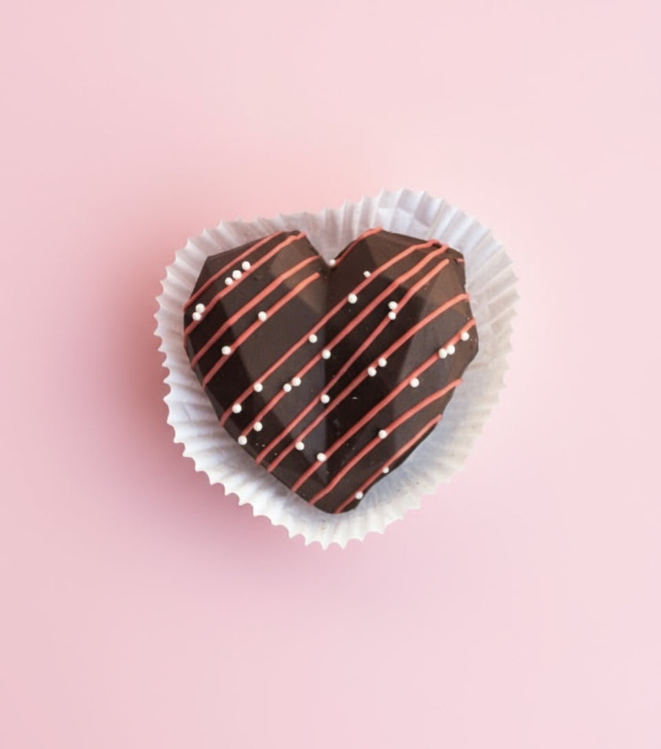 Heart-shaped chocolate treat with white and red drizzle on a pink background