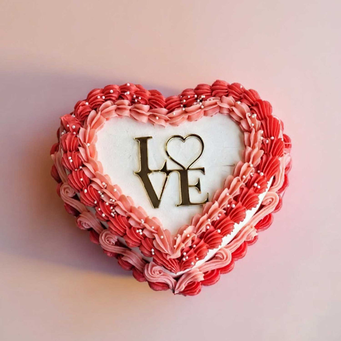 Heart-shaped cake with red and pink frosting and 'I LOVE' text on a soft pink background