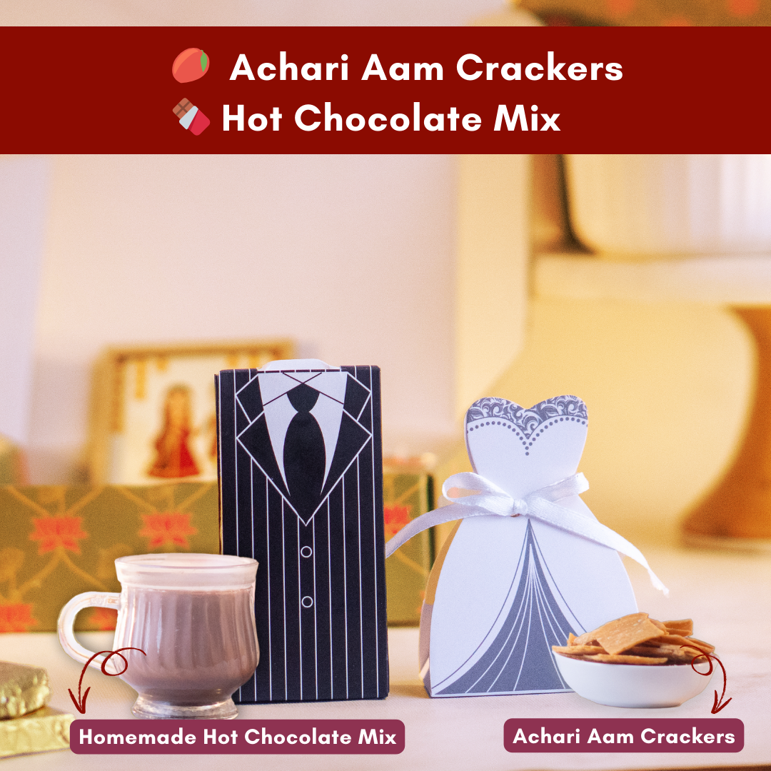 a close up direct shot of a tuxedo groom box with a cup of homemade hot chocolate and a white bride dress with a cup of achari aam crackers 