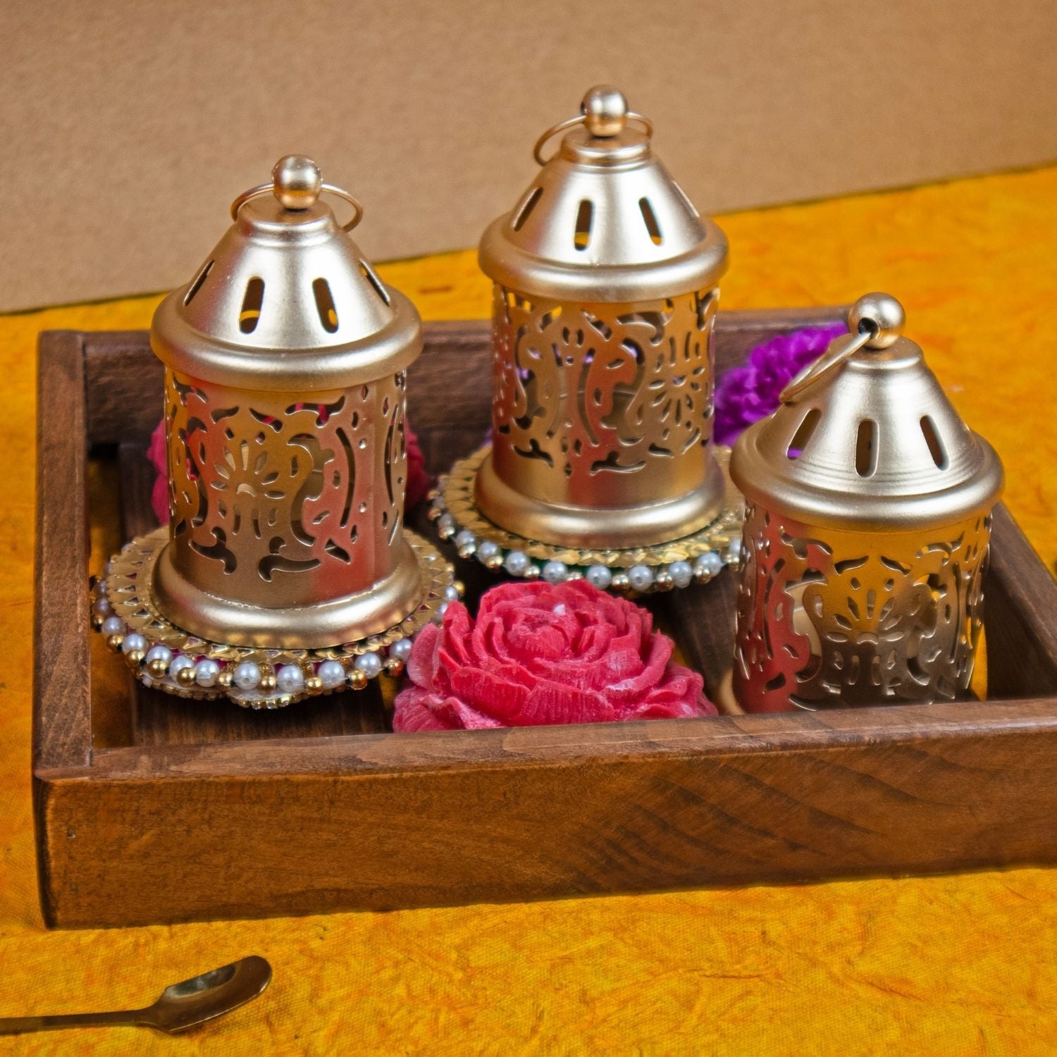 Decorative metal lanterns with floral elements on a wooden tray against a yellow background