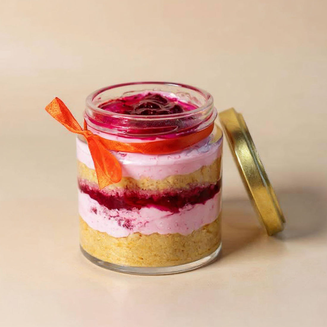 Layered dessert in a glass jar with a gold lid on a beige background