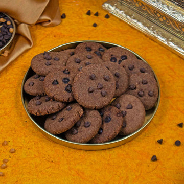 Ragi cookies with chocolate chips in a metal tin on an orange surface.