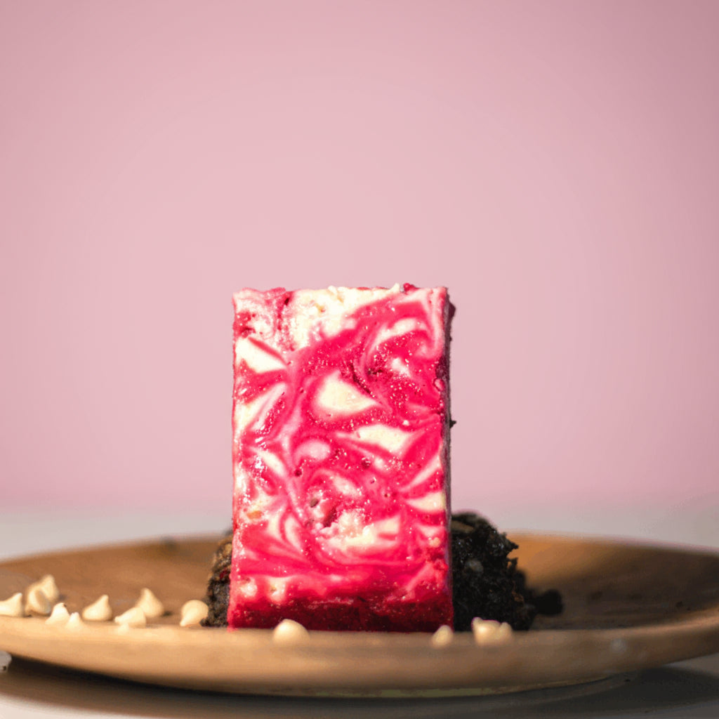 Pink and white marbled red velvet brownie on a wooden plate with a pink background
