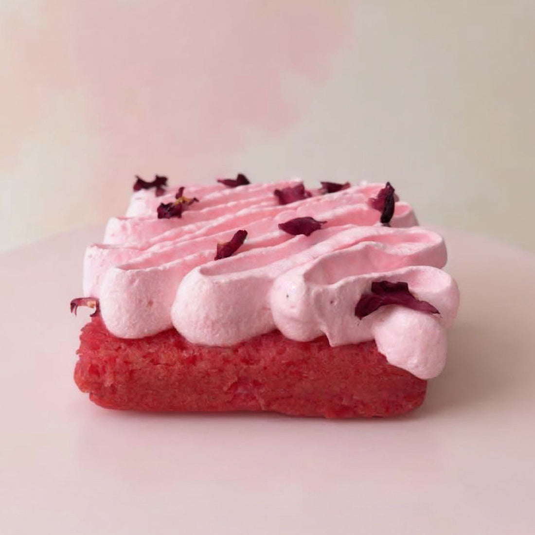 Pink and red cake with white frosting and purple flowers on a light pink background