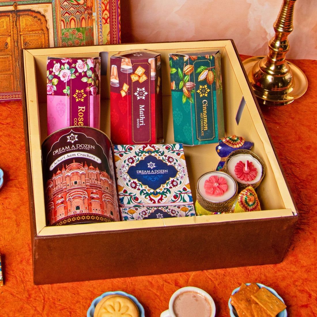 Assorted tea boxes in a decorative box with a traditional book and brass lamp on an orange surface.