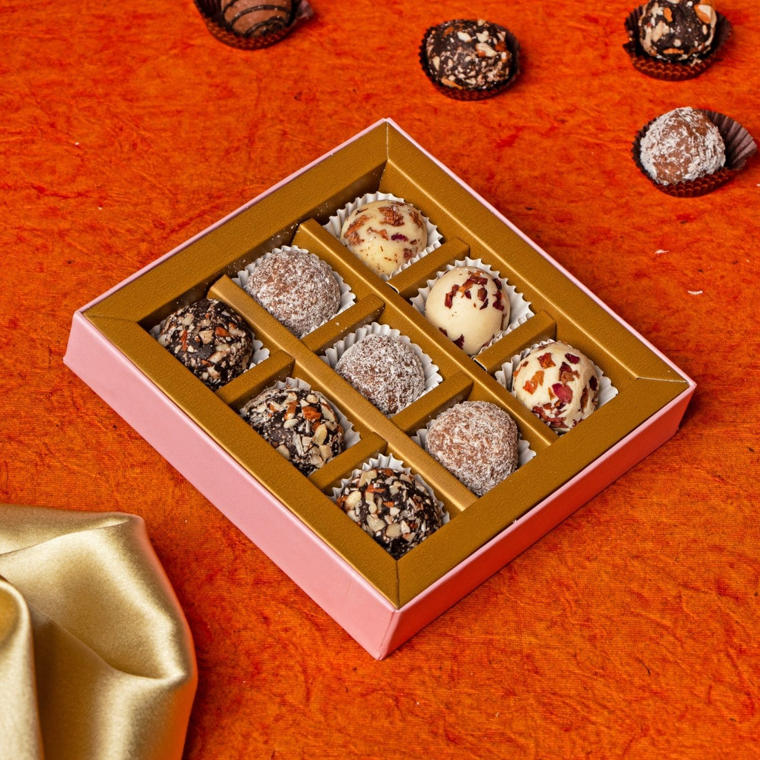 Box of assorted chocolates on an orange surface with a gold satin cloth.