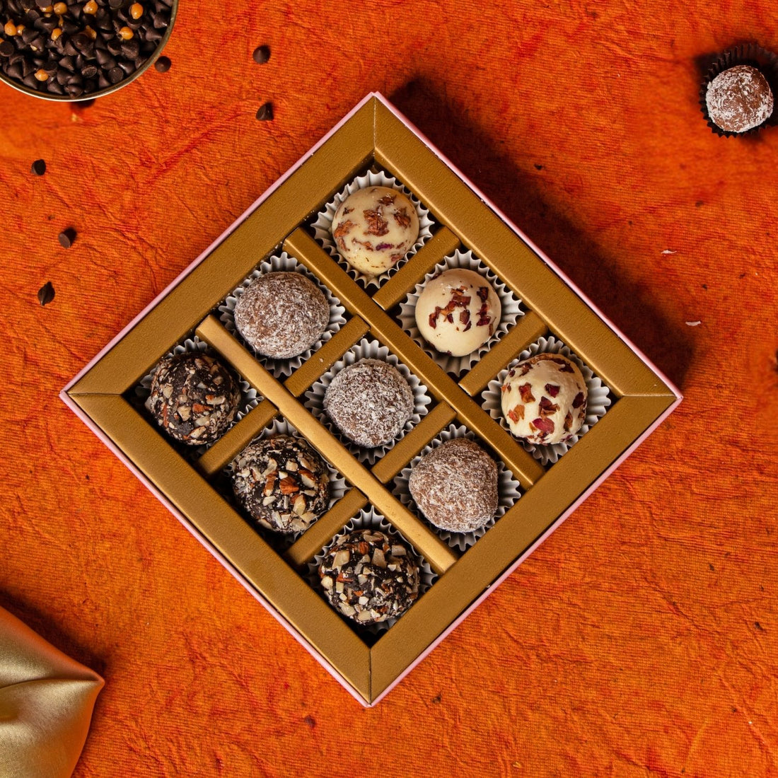 Box of assorted chocolates on an orange surface with a gold satin cloth.