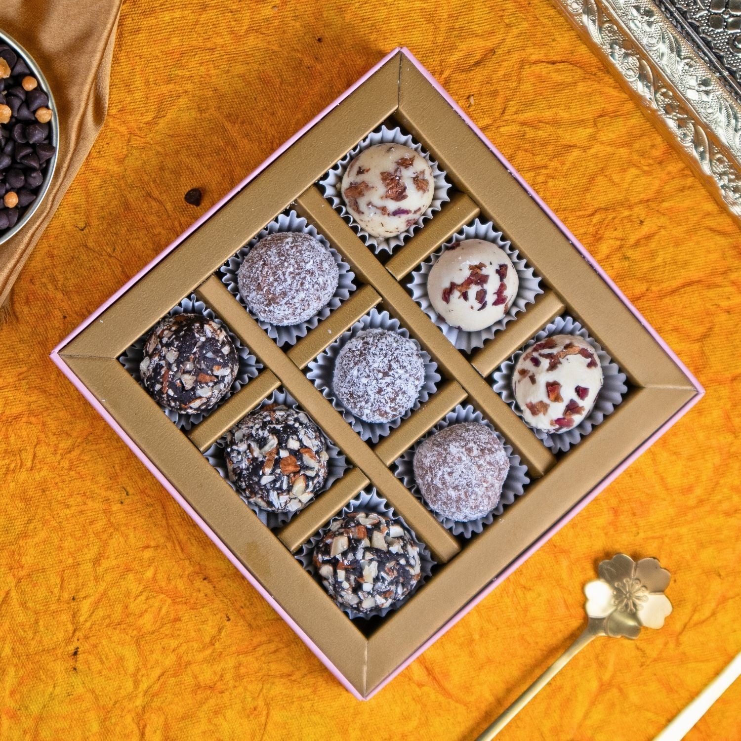 Box of assorted truffles on an orange surface with a decorative spoon.