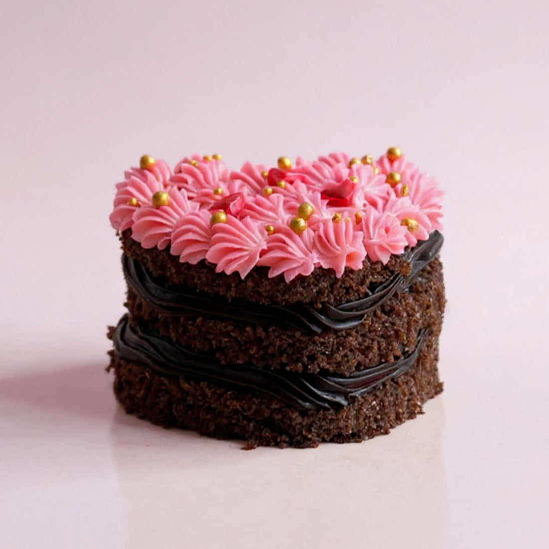 Small chocolate cake with pink frosting and gold sprinkles on a light pink background